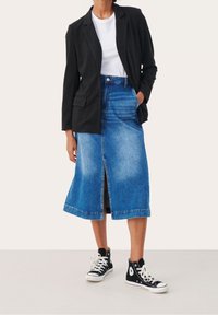 Blazer a scacchi neri sopra una maglietta bianca, abbinato a una gonna di jeans blu lungo il ginocchio con uno spacco frontale e sneakers nere alte.
