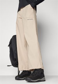Beige Columbia hiking pants with wide legs, featuring two side pockets and elastic cuffs, paired with black rugged hiking boots.