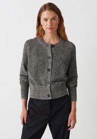 Cardigan grigio strutturato con scollo rotondo, bottoni frontali e maniche lunghe, realizzato in materiale lavorato a maglia. Viene indossato con pantaloni neri.