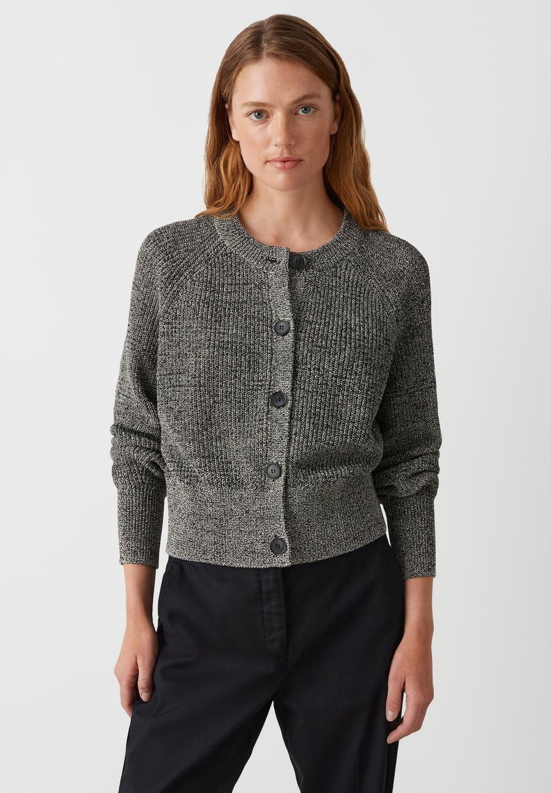 Cardigan grigio strutturato con scollo rotondo, bottoni frontali e maniche lunghe, realizzato in materiale lavorato a maglia. Viene indossato con pantaloni neri.
