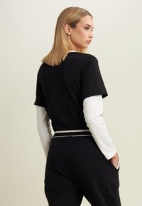 Top nero a maniche corte sovrapposto a una camicia bianca a maniche lunghe, con vita aderente e striscia orizzontale a contrasto in vita.
