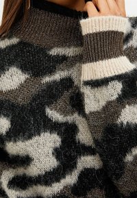 Maglione a maglia con un motivo mimetico nero, marrone e bianco, dotato di colletto e polsini a coste. Tessuto morbido e testurizzato con una leggera lucentezza.
