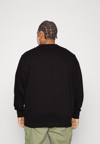 Svart sweatshirt med långa ärmar och ribbade manschetter. Baksidan har en enkel design utan ytterligare mönster eller accenter.