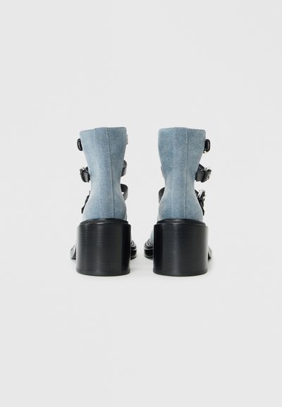 Denim ankle boots with black heels; features adjustable buckles and a structured design. Blue denim top with smooth black accents.