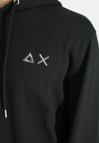 Felpa nera con cappuccio realizzata in tessuto misto cotone, dotata di cappuccio con cordino e logo geometrico ricamato in argento sul petto.