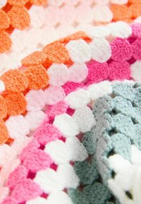 Couverture au crochet avec des sections texturées en orange, rose, blanc et gris. Le motif met en valeur des points surélevés ressemblant à des bulles.