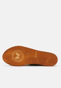 Suela de zapato de madera marrón con una impresión de logo redondo, que presenta una forma de corazón. Textura suave con un ligero brillo, mostrando signos de desgaste.
