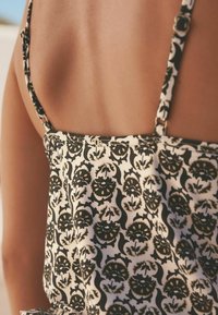 Tissu noir et doré à motifs sur un vêtement aux fines bretelles, avec une texture douce et un design ajusté au niveau du dos.