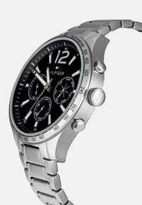 Montre chronographe avec un cadran noir, des index argentés et un bracelet en acier inoxydable. Présente trois sous-cadrans et une lunette tachymétrique.