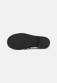 Semelle d'une chaussure noire avec une surface antidérapante texturée, taille 37, vue par le dessous sur un fond blanc uni.