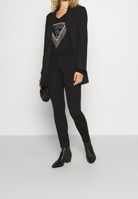 Musta bleiseri mustan, hopeakoristeisen topin päällä, yhdistettynä mustiin leggingsseihin ja nilkkureihin, korostaen tyylikästä siluettia.