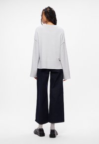 Ανοιχτό γκρι, φαρδύ πουλόβερ με χαμηλούς ώμους, συνδυασμένο με σκούρα παντελόνια με φαρδιά πόδια. Υφασμάτινη υφή, άνετη εφαρμογή και μαύρα υποδήματα αντίθετης απόχρωσης.