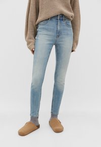 Light blue, high-rise skinny jeans with a faded finish. Paired with a beige knit sweater and brown clogs. Simple design and form-fitting.