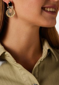 Gouden oorbellen met een zonnestralenontwerp, voorzien van een donkere edelsteen bovenop en heldere accentstenen, die fijne details en vormen tentoonstellen.