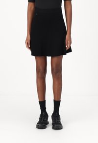 Falda negra de punto acanalado con cintura ceñida, con dobladillo ligeramente acampanado, combinada con zapatillas deportivas negras y calcetines largos negros.