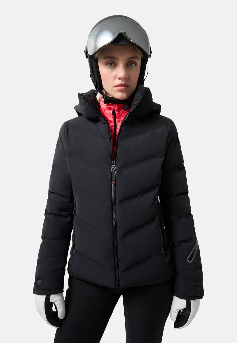 Schwarze Puffjacke mit Reißverschluss vorne, Kapuze und seitlichen Taschen. Getragen mit einer rosa Innenschicht, weißen Handschuhen und einem silbernen Helm.