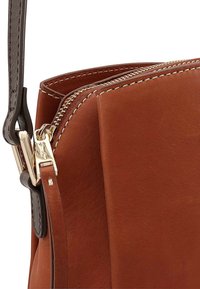 Bruine leren handtas met een gouden rits, met een contrasterende zwarte schouderriem en witte stiksel. Gladde textuur met een gestructureerd ontwerp.