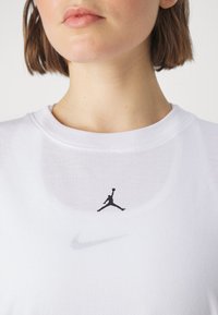 Hvitt sportslig skjorte med strukturert stoff. Har en svart Jumpman-logo og en subtil Nike swoosh på forsiden.