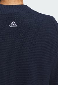 Marineblauer, gestrickter Pullover mit einer strukturierten Oberfläche. Verfügt über einen gerippten Kragen und ein weißes, gesticktes Logo auf der Rückseite.