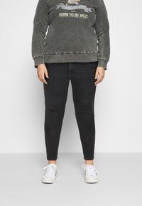 Šedá mikina s grafikou "Born to be Wild" spojená s černými skinny džíny a bílými teniskami; neformální outfit s výrazným barevným kontrastem.