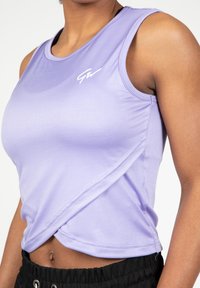 Paarse sportieve tanktop gemaakt van zachte, rekbare stof. Heeft een ronde halslijn en een subtiel logo op de borst. Verkorte pasvorm.