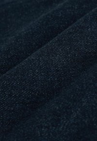Tissu bleu foncé avec une texture tissée visible et des fibres fines, présenté en gros plan avec des plis doux et des ombres.