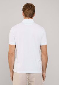Chemise polo blanche à manches courtes, col plat, avec des accents bleu clair sur le col et les bords des manches. Texture en coton lisse.