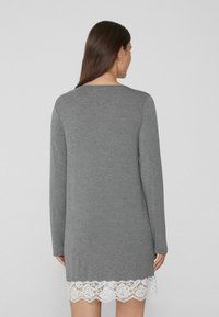 Vestido suéter gris con mangas largas y un borde de encaje floral en el dobladillo. Textura suave y corte relajado.