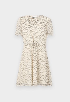 Īsām piedurknēm, V-veida kakla kleita gaisā bēšā krāsā ar tumši brūniem neregulāriem punktiem. Pasvītrota ar cinch jostu ar saišu detaļu, izgatavota no plūstoša auduma.