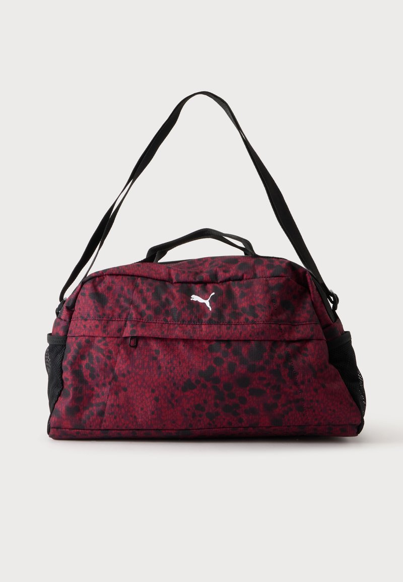 Sac de sport rouge et noir à pois avec poche zippée à l'avant, poches latérales en mesh noir, double poignées et bandoulière réglable.