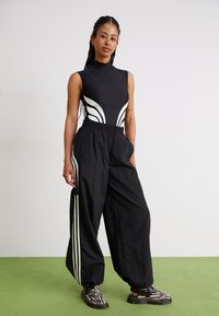 Svart ermeløs bodysuit med hvite sidelister, parret med løse svarte bukser med hvite sidelister og teksturerte svart-hvite sko.