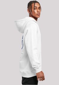 White hooded sweatshirt with a kangaroo pocket, featuring a large blue graphic design on the front. Ribbed cuffs and hem detail.
