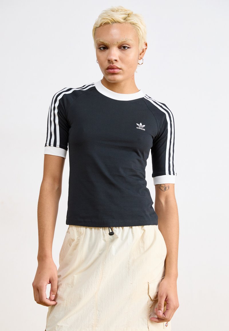Svart kortermet t-skjorte med hvite detaljer og tre hvite striper på hver skulder; har Adidas-logoen i hvitt.