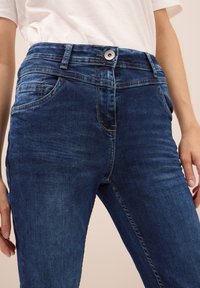 Donkerblauwe denim jeans met een gladde textuur, vijfzakkenontwerp, een ritssluiting en een enkele knoopsluiting bij de taille.