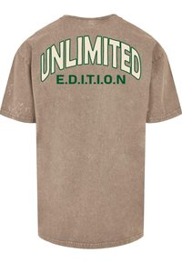 Brun kortermet t-skjorte med fet, buet "UNLIMITED" tekst i krem og "E.D.I.T.I.O.N" under i grønt, med en teksturert finish.