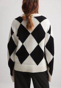 Strickpullover mit einem Diamantmuster in Schwarz und Creme. Lockere Passform mit geripptem Saum und Ärmelbündchen, strukturiertem Stoff und weiten Ärmeln.