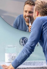 Elektrische tandenborstel met een witte handgreep en grijze accenten, geplaatst op een marmeren aanrecht naast een transparante waterflosser. Spiegelreflectie zichtbaar.
