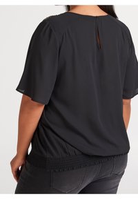 Svart blus med korta ärmar, slät textur och smockad nederkant. Baksidan har en nyckelhålöppning vid halsringningen för extra detalj.