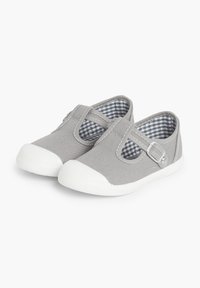 Zapatos de lona grises con un diseño de tira en T, que incluye una hebilla plateada. El interior tiene un patrón de cuadros azul y blanco. Suelas de goma blancas.