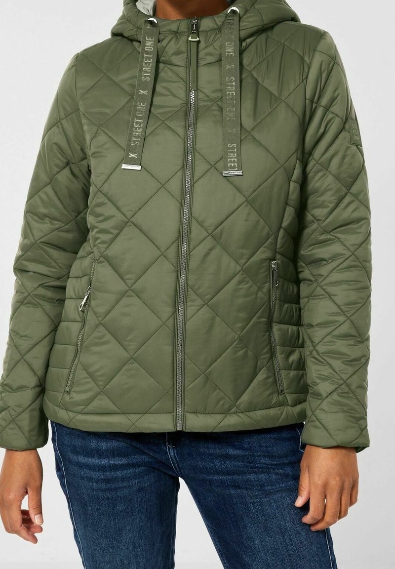 Giacca verde trapuntata con cappuccio, dotata di chiusura frontale con cerniera, coulisse in tessuto e tasche laterali. Il materiale sembra liscio e leggero.