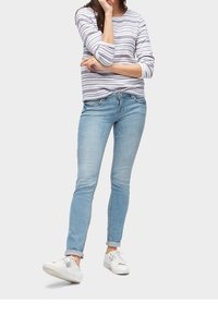 Jeans de denim azul con corte ajustado, combinados con una camisa de rayas de manga larga en gris claro y blanco, y zapatillas blancas.