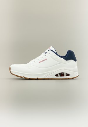 Λευκό αθλητικό παπούτσι Skechers με ναυτικό γιακά, κόκκινο λογότυπο στο πλάι και στη γλώσσα, διάτρητες λεπτομέρειες και καφέ λαστιχένια εξωτερική σόλα με ορατό αερόσακο.