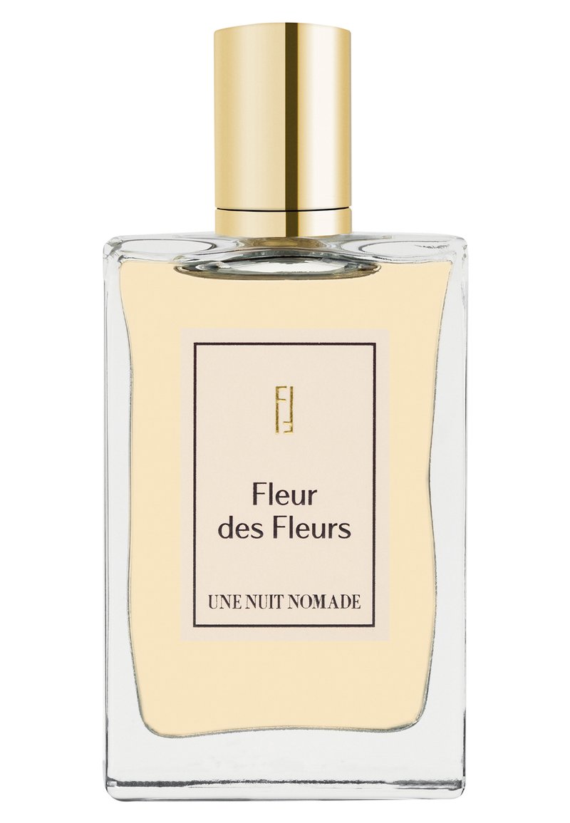 Rechteckige klare Glasparfümflasche mit hellgelber Flüssigkeit, goldenem Verschluss und Etikett mit der Aufschrift "Fleur des Fleurs UNE NUIT NOMADE."