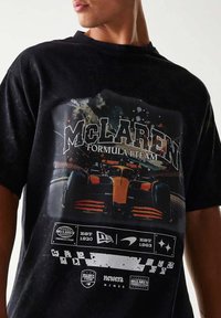 Czarny t-shirt bawełniany z grafiką samochodu wyścigowego McLaren Formula 1. Projekt zawiera kolorowe plamy farby oraz logotypy marek.