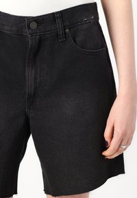 Shorts en denim noir à taille haute, design à cinq poches, ourlet brut et fermeture à bouton à la taille. Texture lisse avec des coutures minimales.