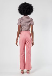 Schwarz-weiß-pinker, gemusterter Kurzarmtop, kombiniert mit hochgeschnittenen, rosa Hosen mit Seitenschlitzen und Gesäßtaschen.