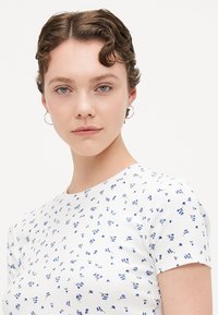Witte textuur top met korte mouwen, met een verspreid blauw bloemmotief. Ronde halsontwerp. De stof lijkt geribbeld en aansluitend.