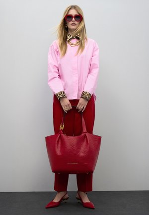 Bolsa de tote texturizada roja con asas anchas, combinada con una camisa rosa, puños con patrón de leopardo y pantalones rojos. Los accesorios incluyen gafas de sol llamativas.