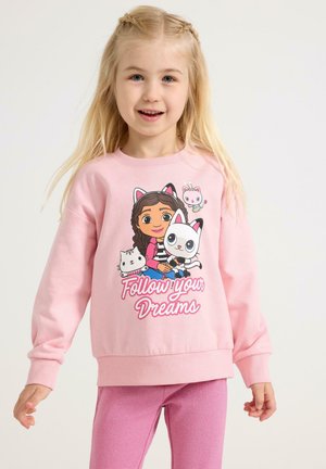 Lichtroze sweatshirt met een cartoonmeisje met katten, tekst "Volg je dromen," en geribbelde manchetten. Gecombineerd met roze legging.