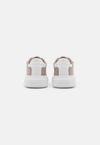 Baskets basses avec une semelle blanche, une tige beige et blanche, une texture en cuir lisse, et un logo embossé sur le talon.